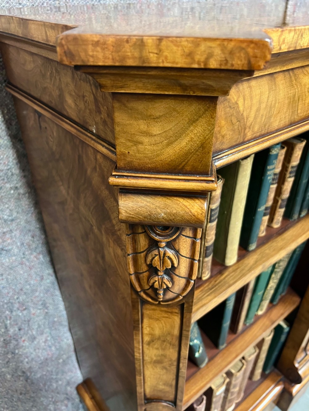 A low, wide Victorian burr walnut open bookcase with three compartmentalised shelf sections, carved pilaster corbels, and a solid plinth base. View VI