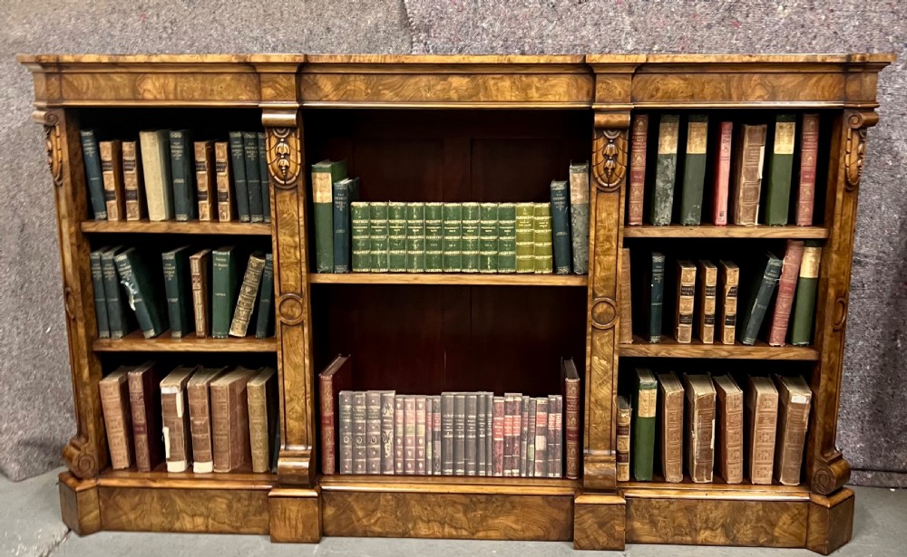 A low, wide Victorian burr walnut open bookcase with three compartmentalised shelf sections, carved pilaster corbels, and a solid plinth base. View IX