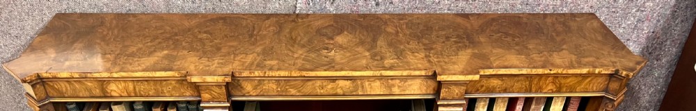 A low, wide Victorian burr walnut open bookcase with three compartmentalised shelf sections, carved pilaster corbels, and a solid plinth base. View XII
