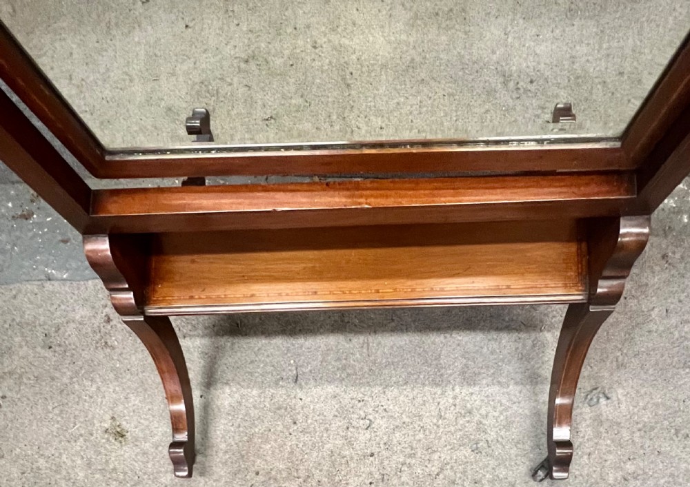 An Edwardian mahogany cheval mirror featuring an arched cresting rail with satinwood line inlay, turned brass finials, bevelled glass plate, and splayed legs on castors. View VI