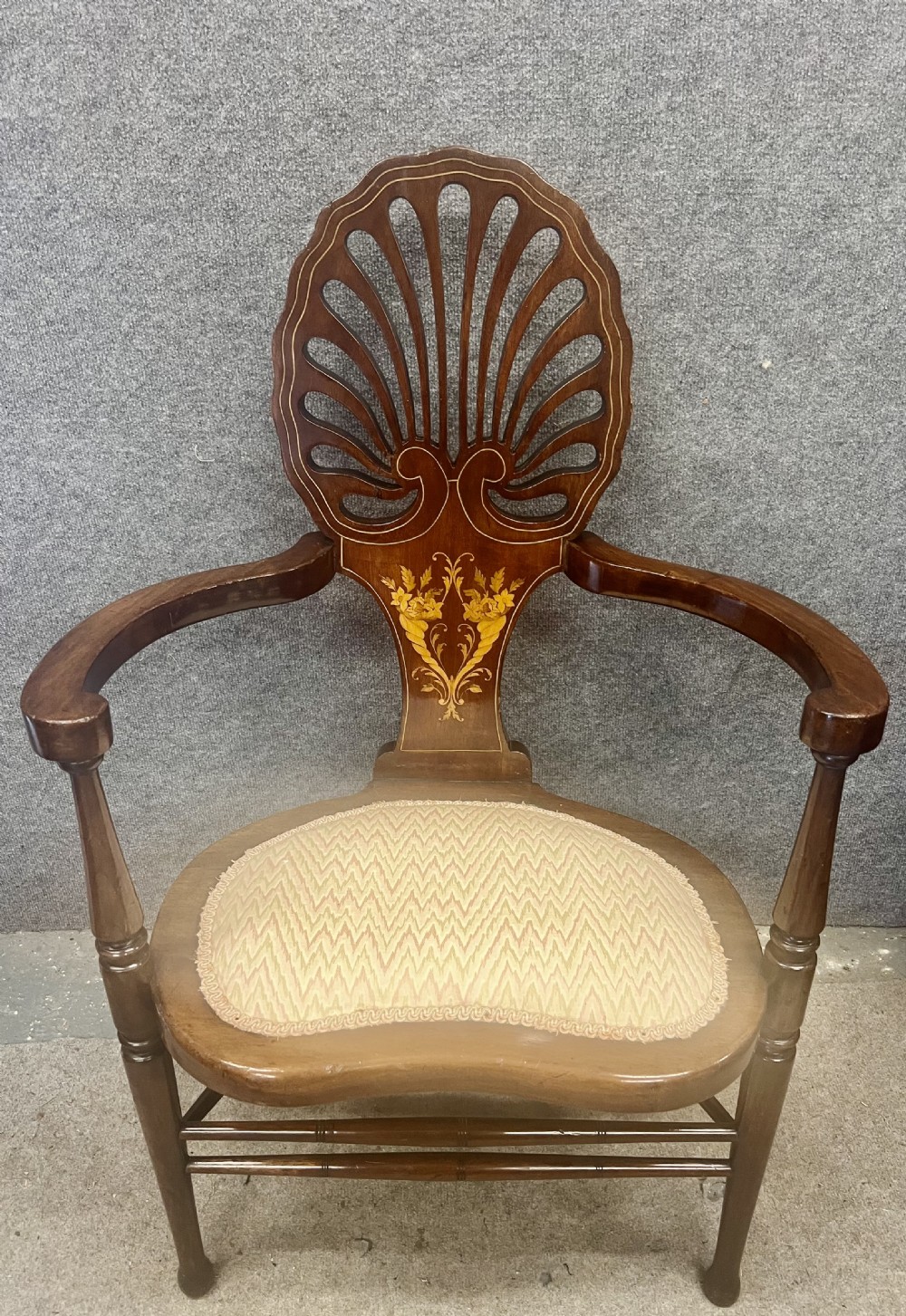 An Art Nouveau mahogany armchair featuring a carved pierced shell backrest, floral marquetry inlay, shaped armrests, and an upholstered seat pad.
