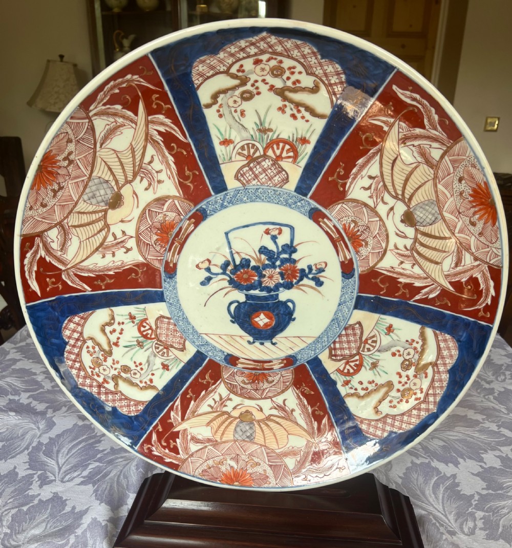 A large circular Japanese Imari porcelain charger featuring radial panelled decoration in cobalt blue, iron red, and white with a central painted flower vase.