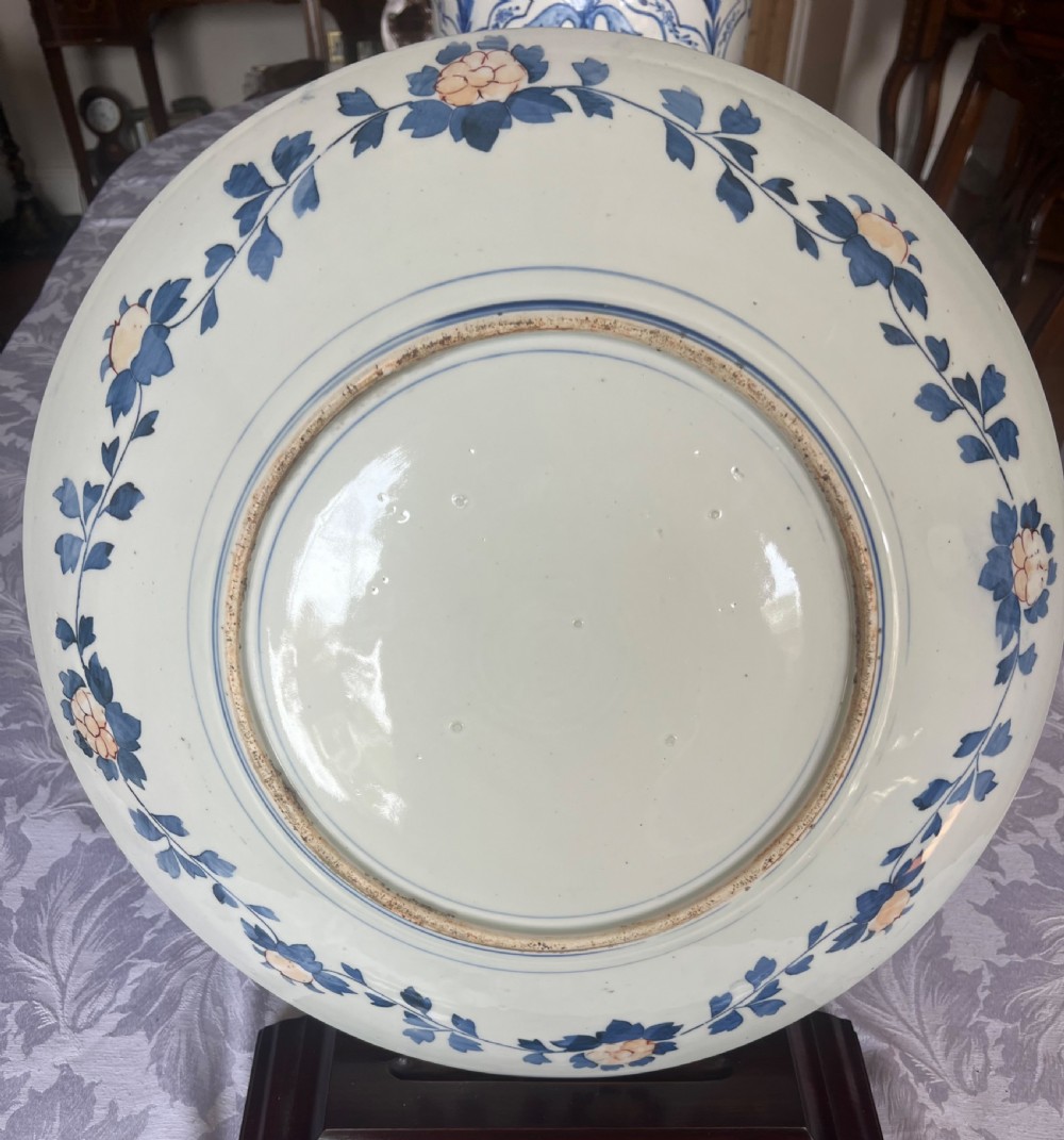 A large circular Japanese Imari porcelain charger featuring radial panelled decoration in cobalt blue, iron red, and white with a central painted flower vase. View II