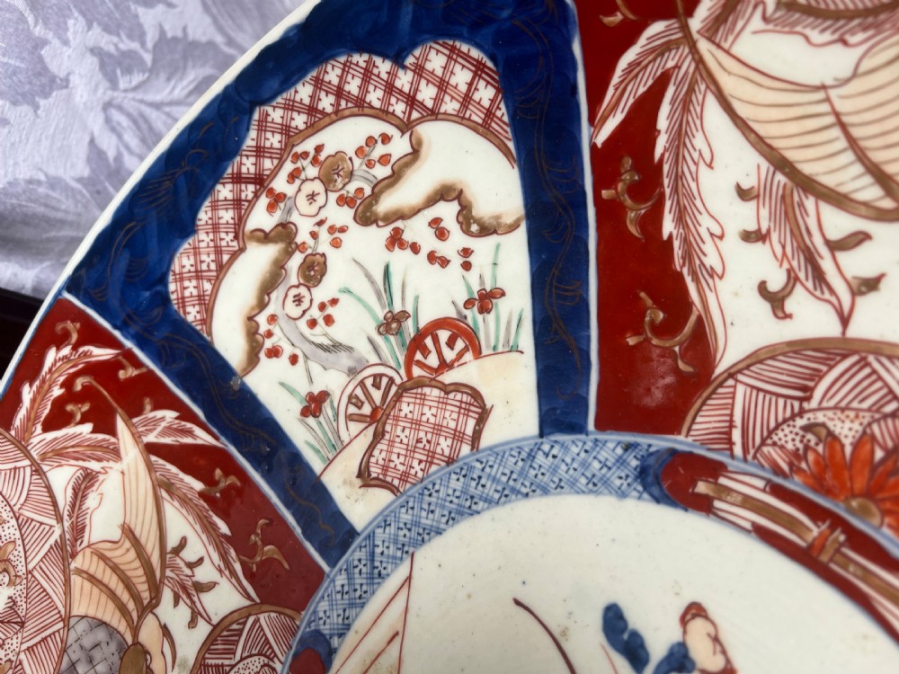 A large circular Japanese Imari porcelain charger featuring radial panelled decoration in cobalt blue, iron red, and white with a central painted flower vase. View III