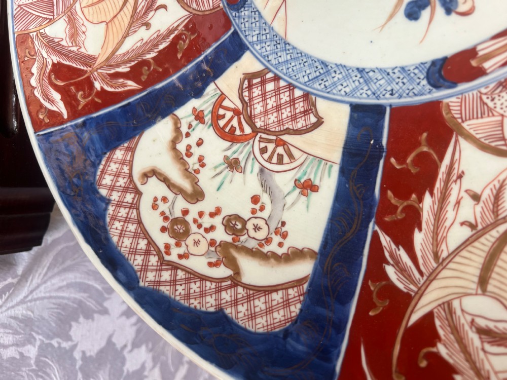 A large circular Japanese Imari porcelain charger featuring radial panelled decoration in cobalt blue, iron red, and white with a central painted flower vase. View V