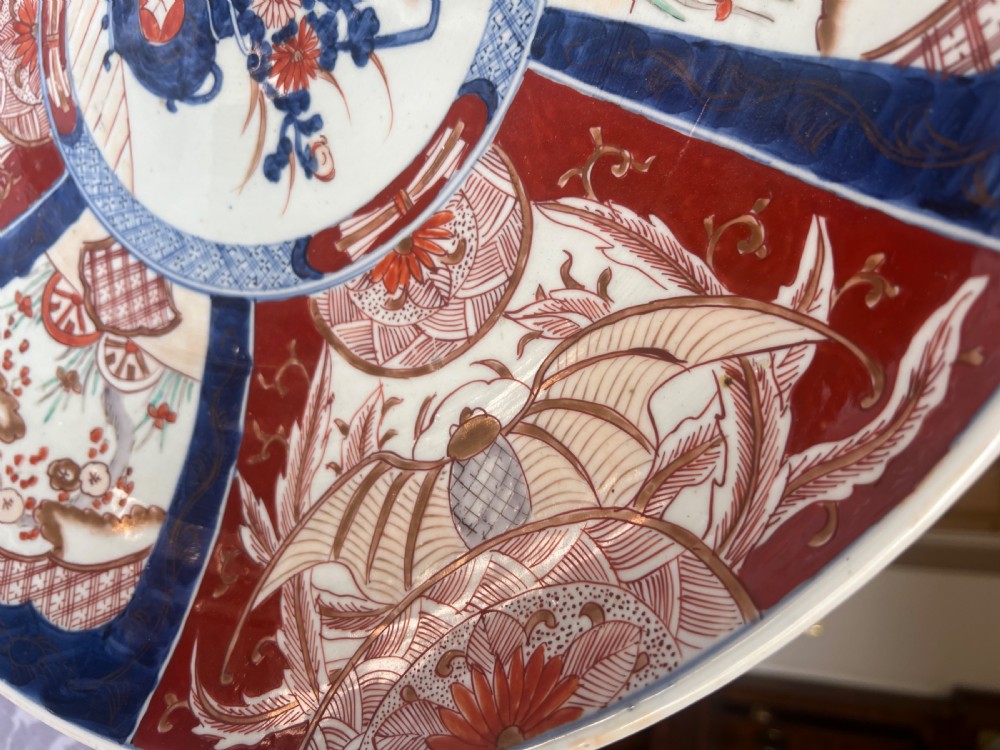 A large circular Japanese Imari porcelain charger featuring radial panelled decoration in cobalt blue, iron red, and white with a central painted flower vase. View VI