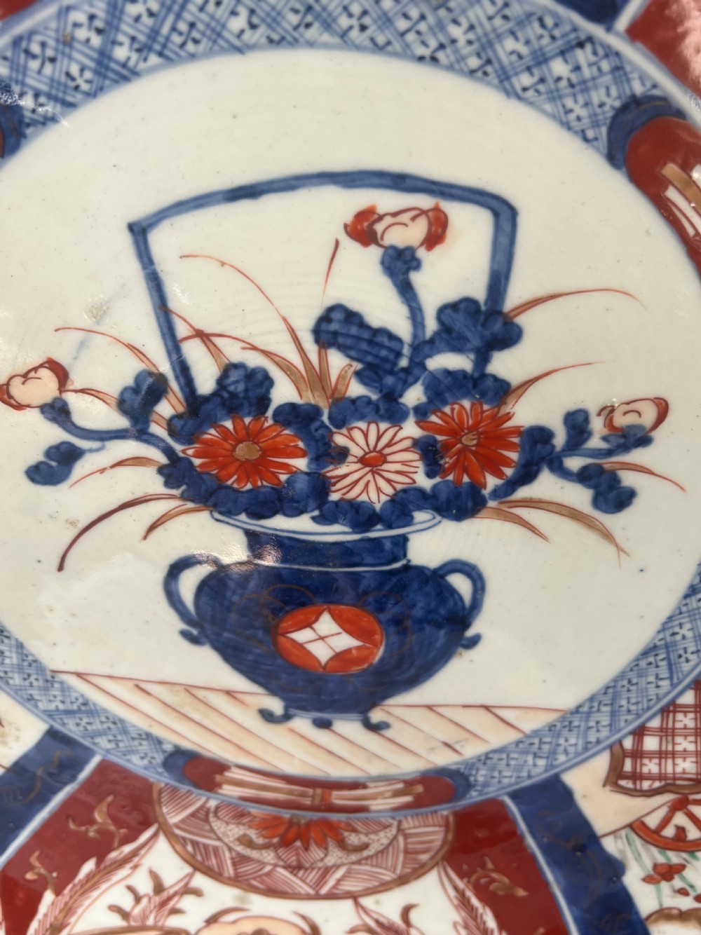 A large circular Japanese Imari porcelain charger featuring radial panelled decoration in cobalt blue, iron red, and white with a central painted flower vase. View VII