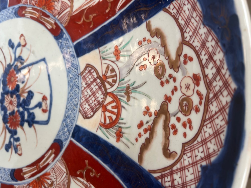 A large circular Japanese Imari porcelain charger featuring radial panelled decoration in cobalt blue, iron red, and white with a central painted flower vase. View IX