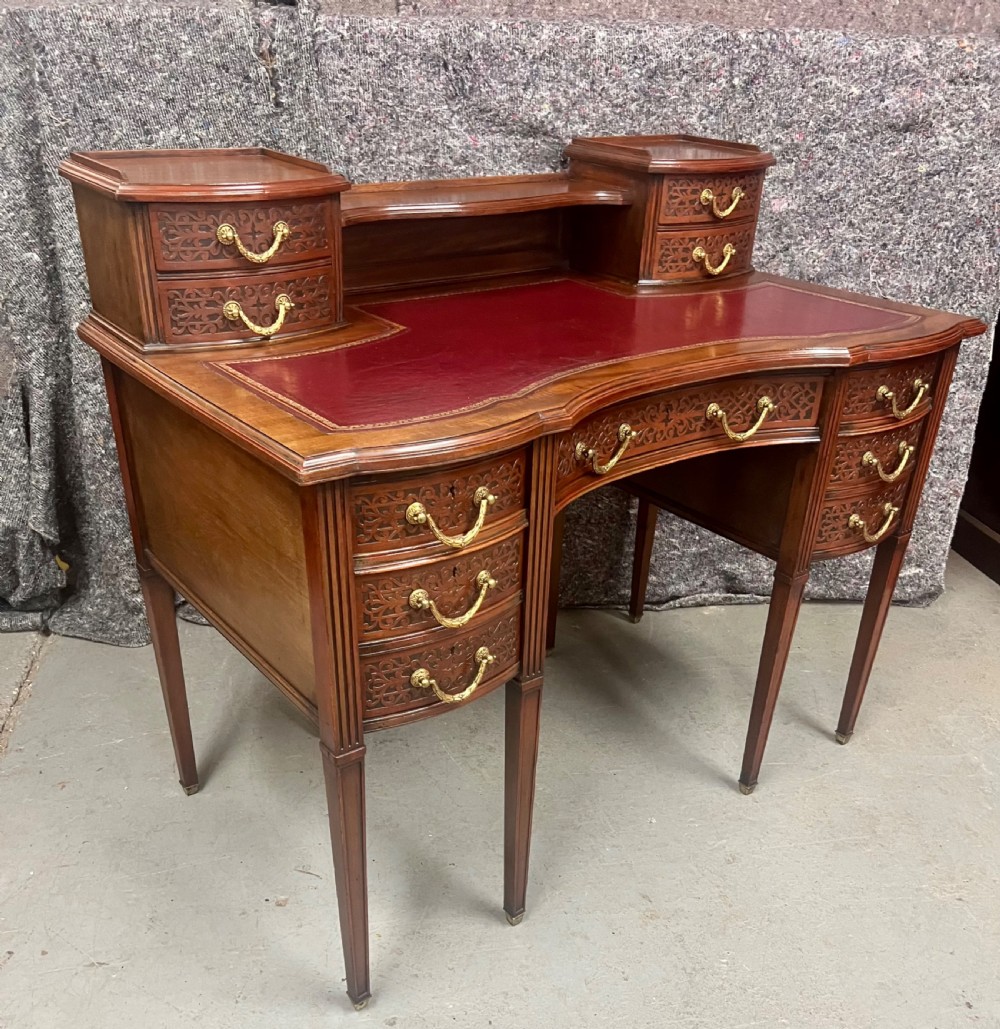 A mahogany writing desk featuring a red leather inset surface, carved drawer fronts, brass swanneck handles, and an elevated superstructure with twin drawer units.