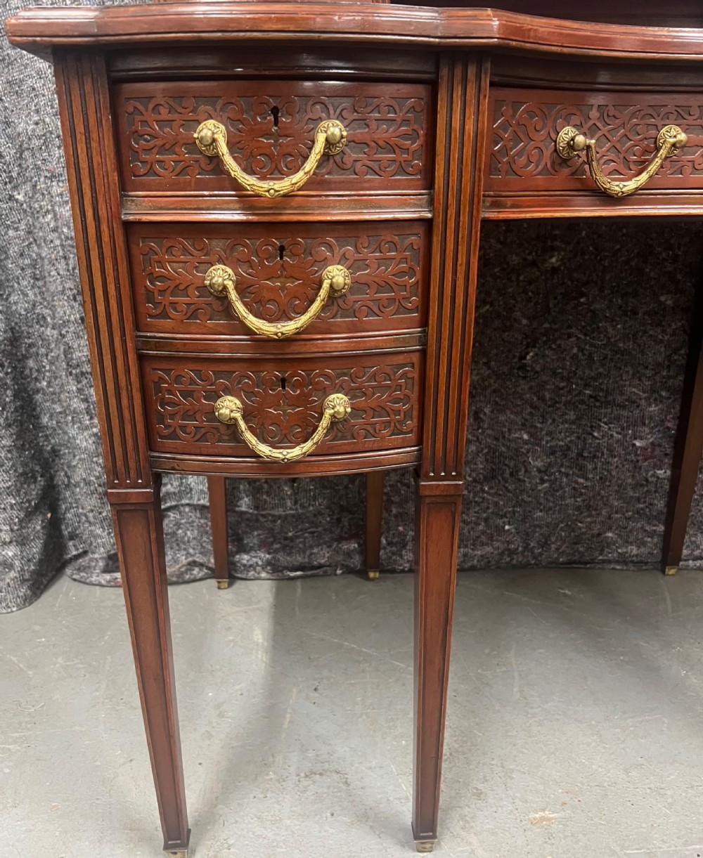 A mahogany writing desk featuring a red leather inset surface, carved drawer fronts, brass swanneck handles, and an elevated superstructure with twin drawer units. View XII