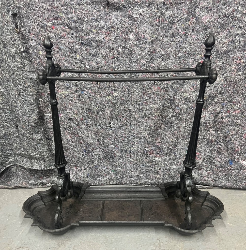 A black Victorian cast iron stick stand featuring twin horizontal support bars, urn finials, rosette mouldings, and a scalloped drip tray base. View II