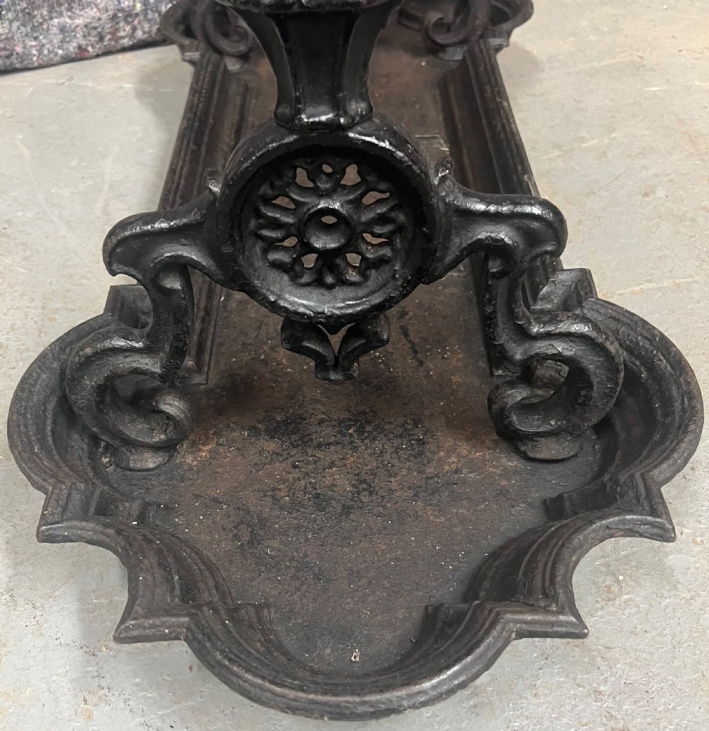 A black Victorian cast iron stick stand featuring twin horizontal support bars, urn finials, rosette mouldings, and a scalloped drip tray base. View IV