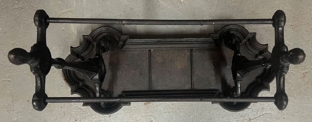 A black Victorian cast iron stick stand featuring twin horizontal support bars, urn finials, rosette mouldings, and a scalloped drip tray base. View VI