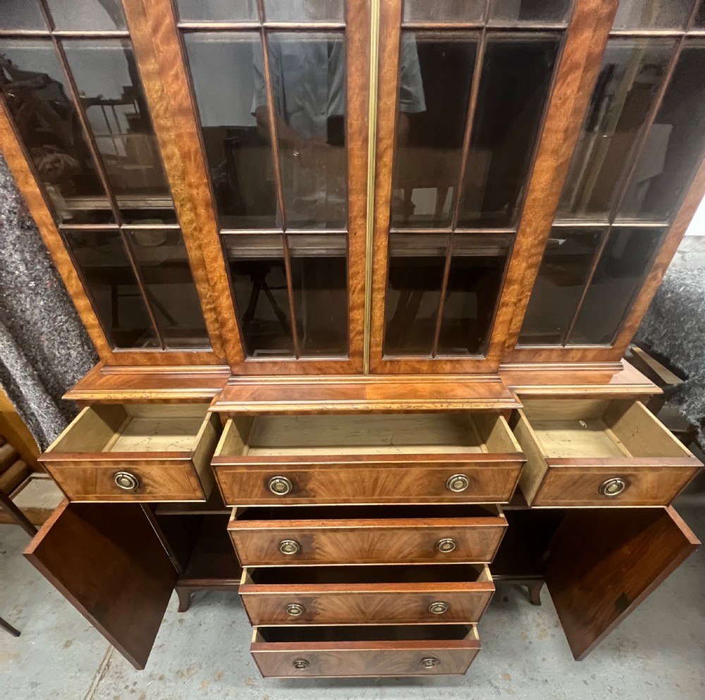 A small Georgian style mahogany breakfront bookcase with upper astragal glazed doors, lower drawers, and oval inlaid cupboard doors. View II