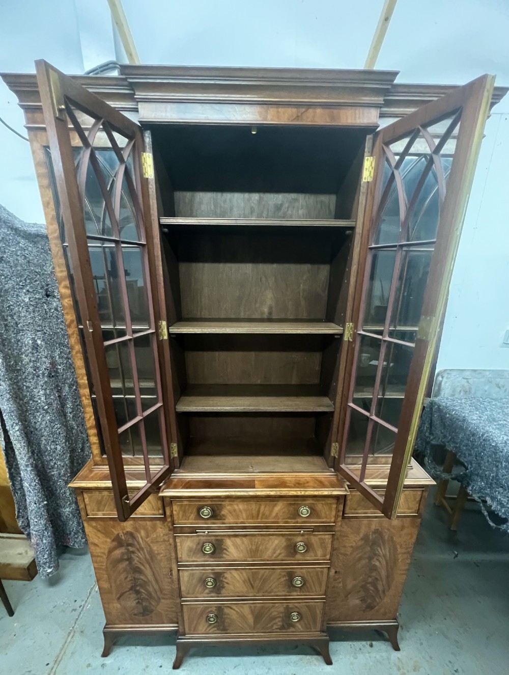 A small Georgian style mahogany breakfront bookcase with upper astragal glazed doors, lower drawers, and oval inlaid cupboard doors. View VI