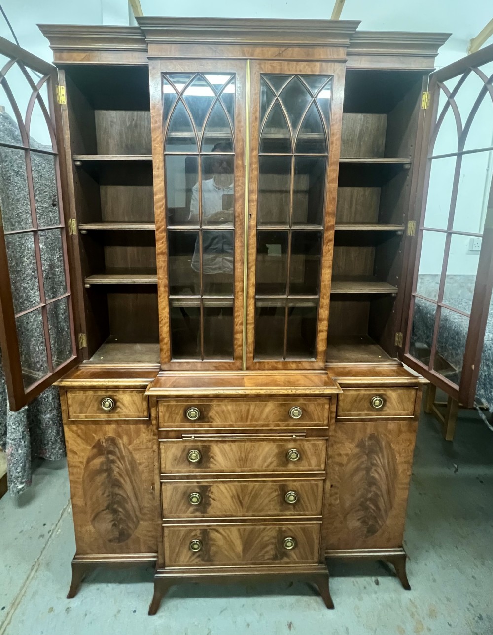 A small Georgian style mahogany breakfront bookcase with upper astragal glazed doors, lower drawers, and oval inlaid cupboard doors. View VII