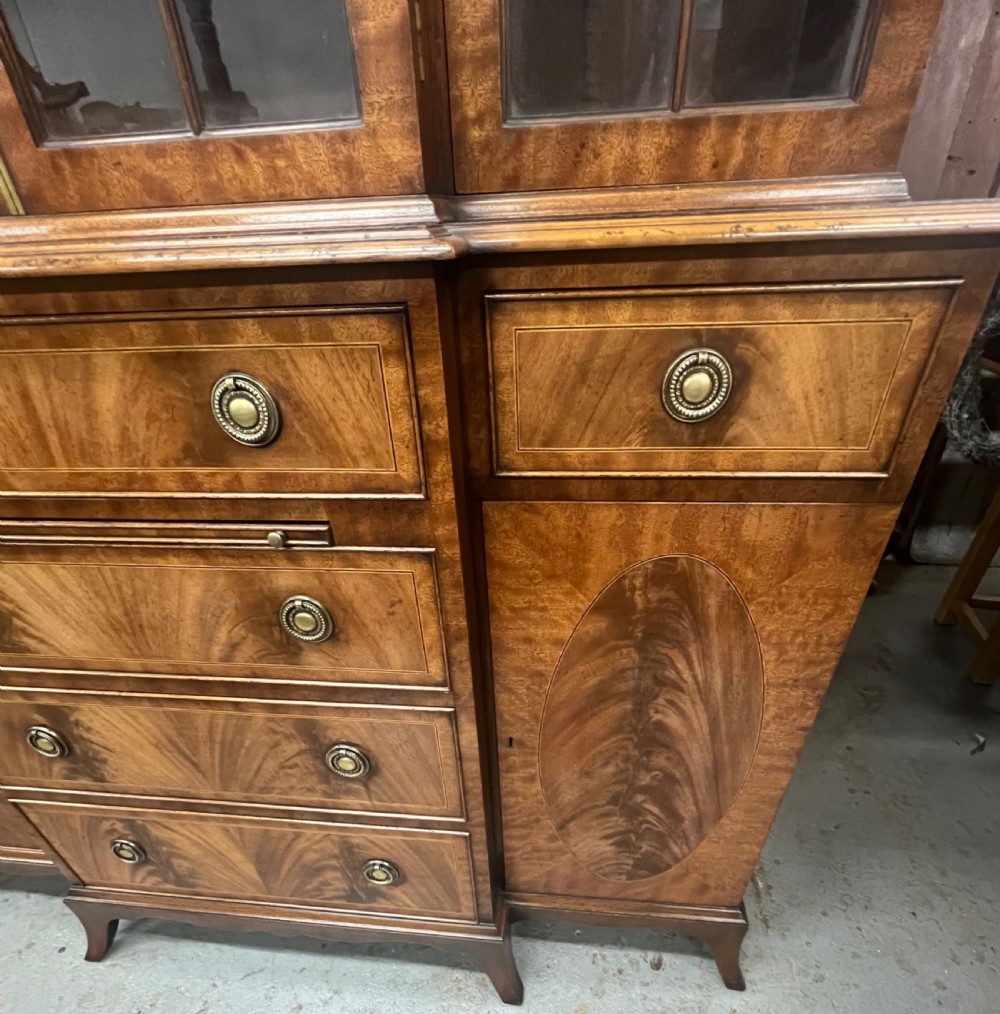 A small Georgian style mahogany breakfront bookcase with upper astragal glazed doors, lower drawers, and oval inlaid cupboard doors. View VIII