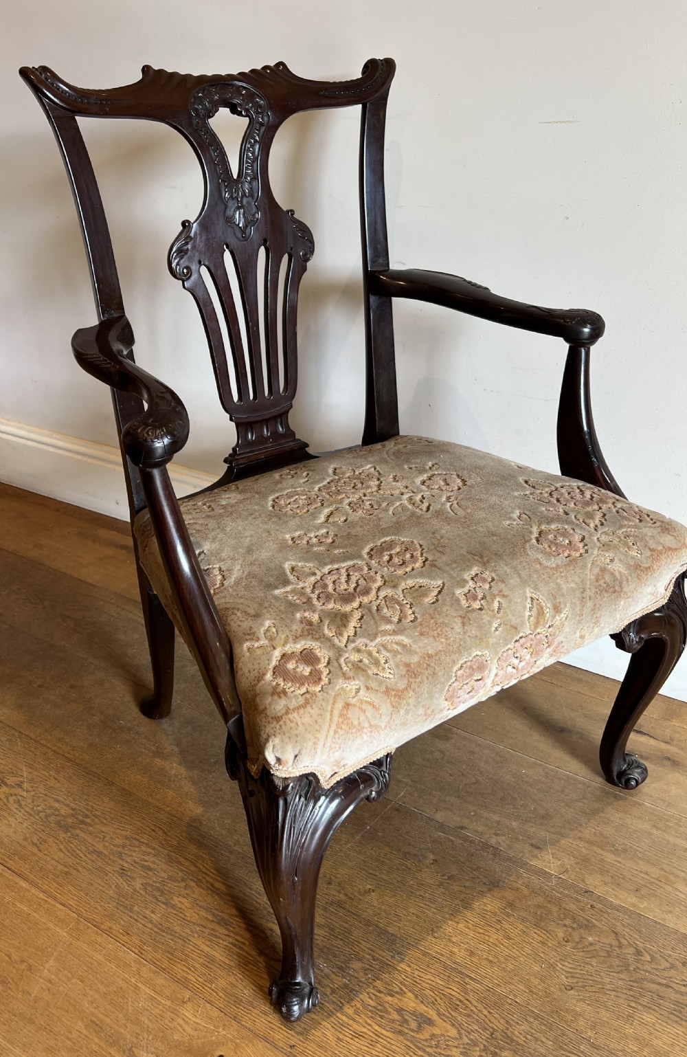 An 18th-century dark mahogany Chippendale armchair featuring a pierced carved back splat, curved arms, floral upholstered seat, and carved cabriole legs.