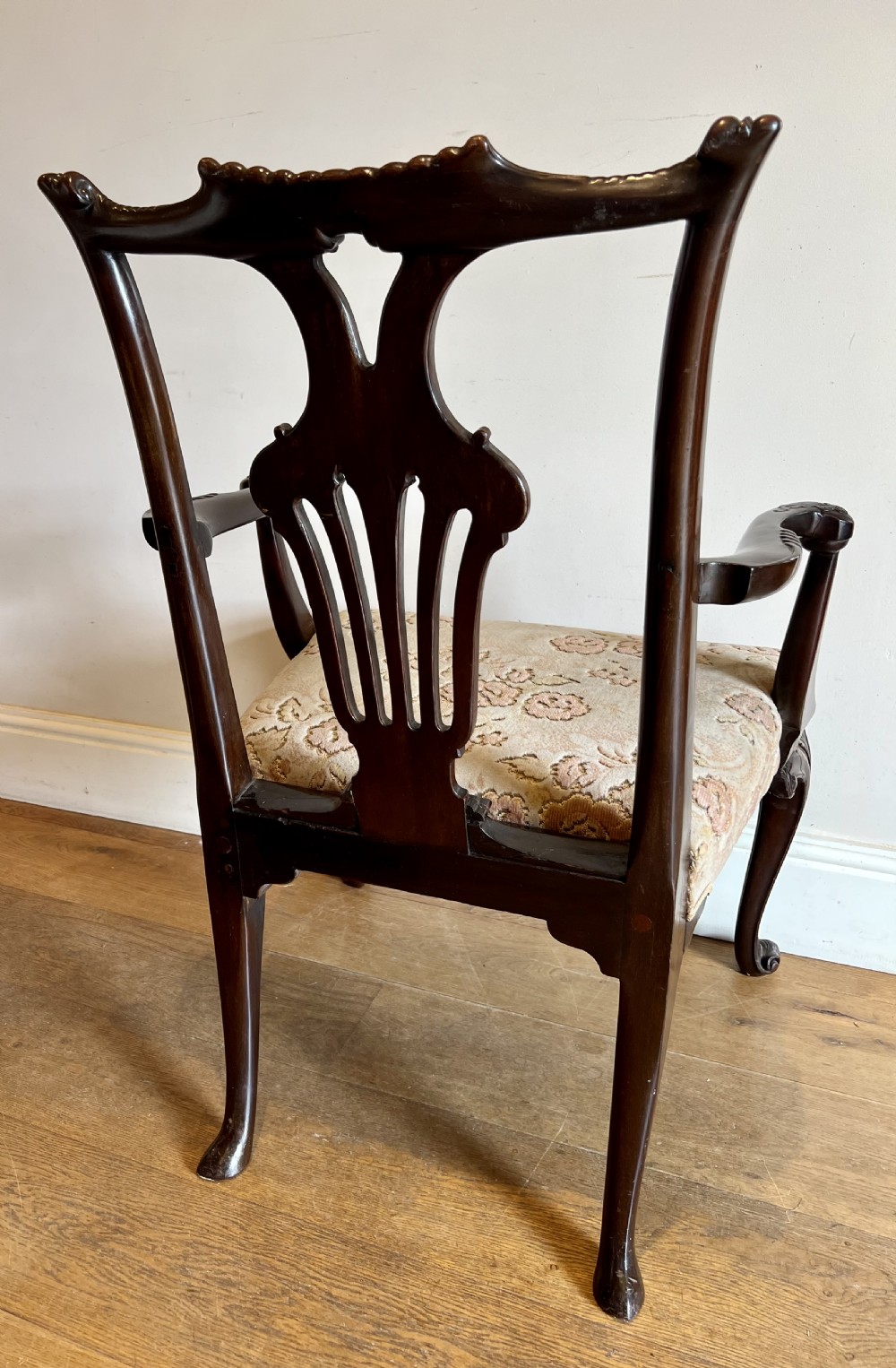 An 18th-century dark mahogany Chippendale armchair featuring a pierced carved back splat, curved arms, floral upholstered seat, and carved cabriole legs. View X