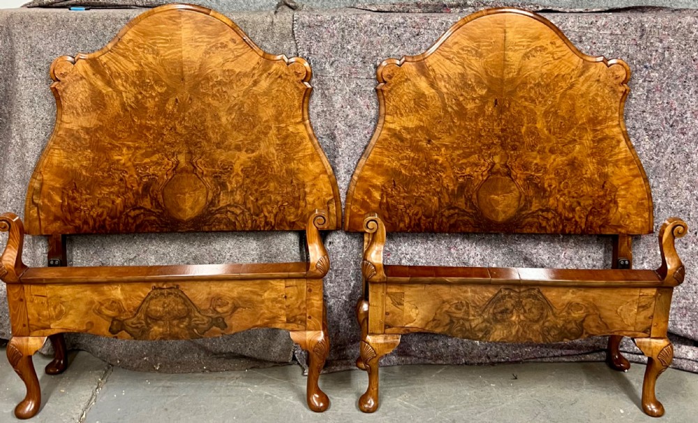A pair of Queen Anne style single bed frames crafted from figured walnut with arched headboards, scrolled footboards, and cabriole legs.
