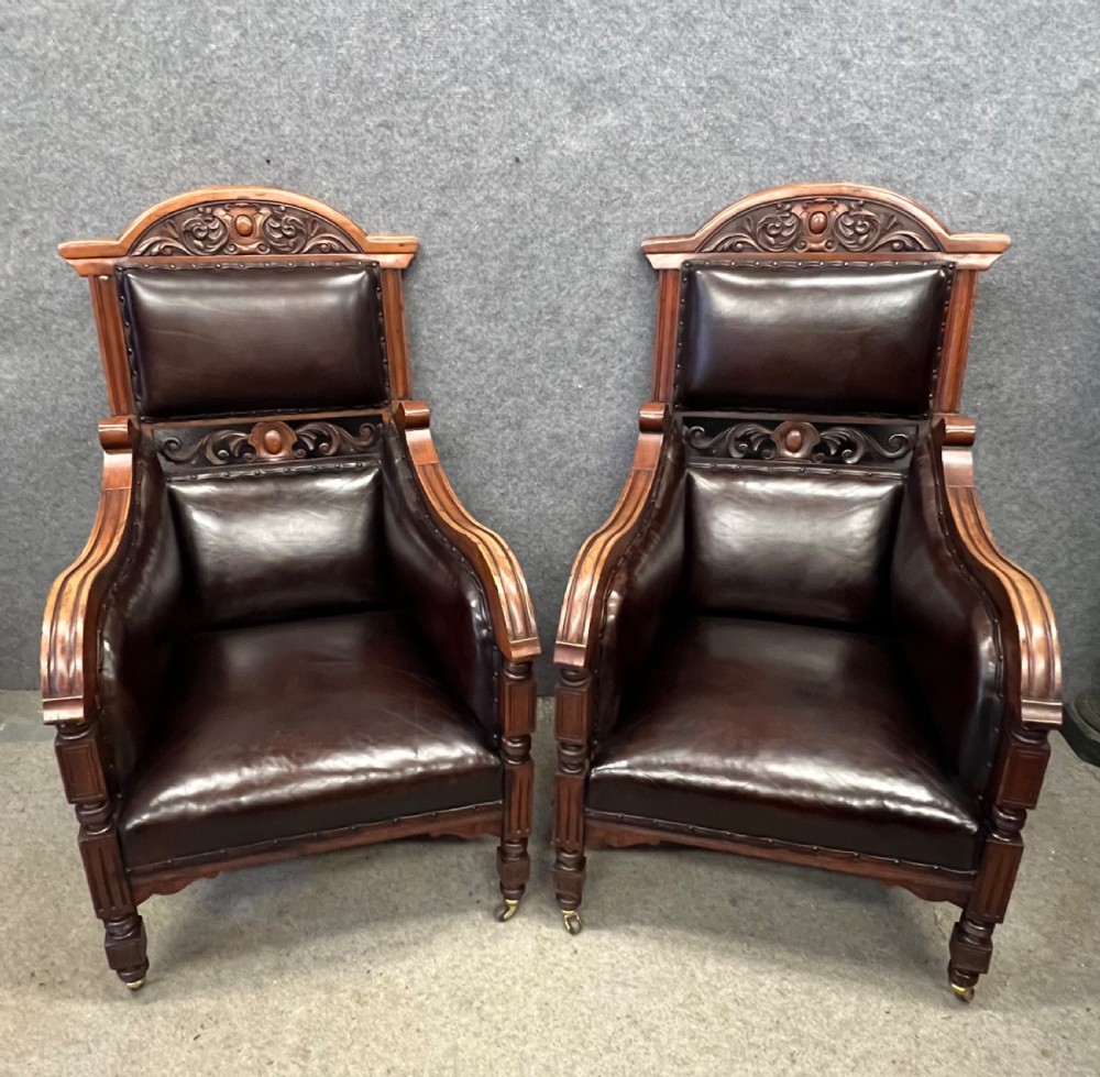 A pair of carved walnut high-back armchairs upholstered in dark brown leather with stud detailing and brass castors.