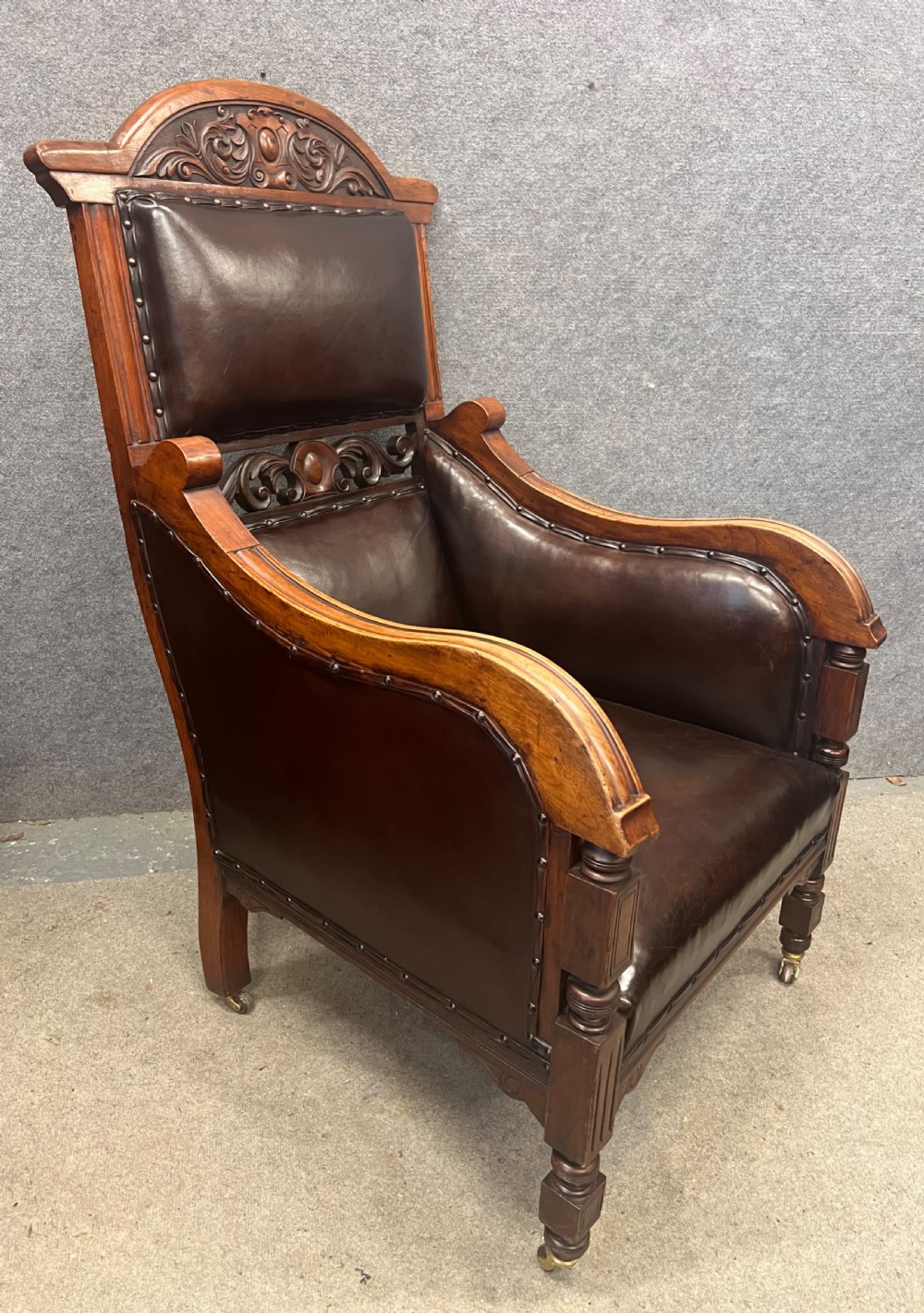 A pair of carved walnut high-back armchairs upholstered in dark brown leather with stud detailing and brass castors. View II