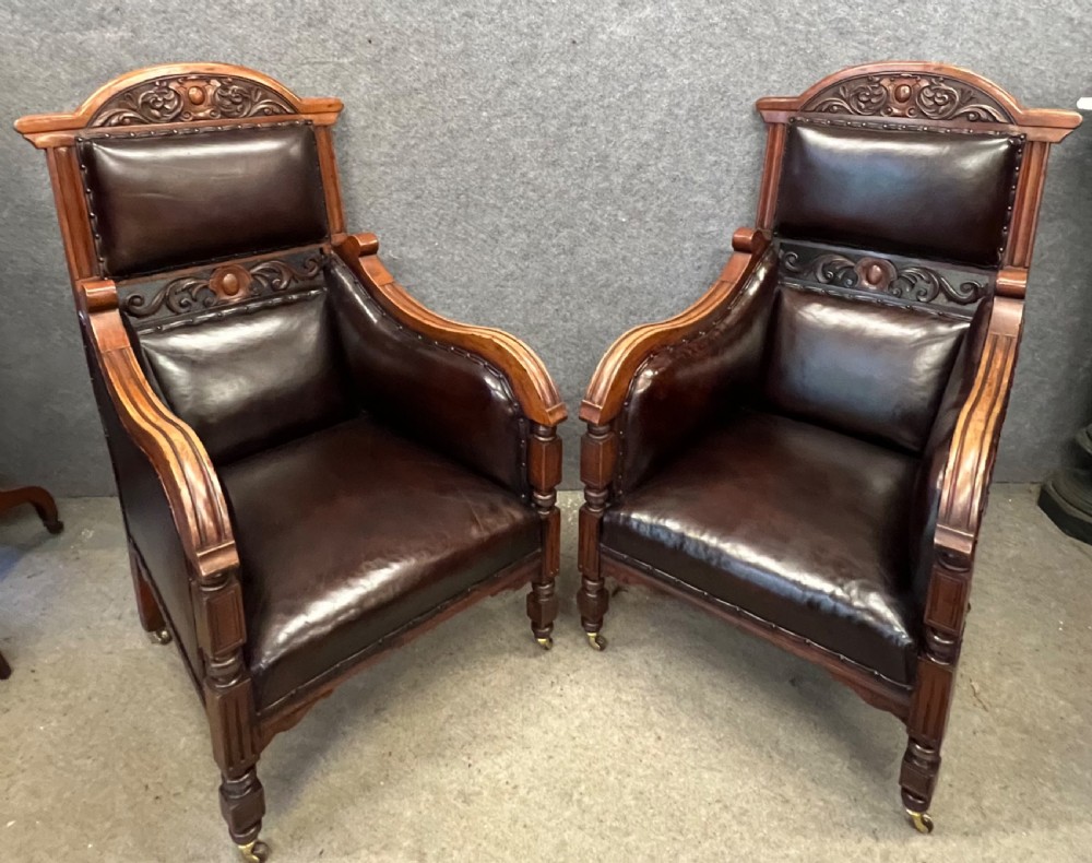 A pair of carved walnut high-back armchairs upholstered in dark brown leather with stud detailing and brass castors. View V