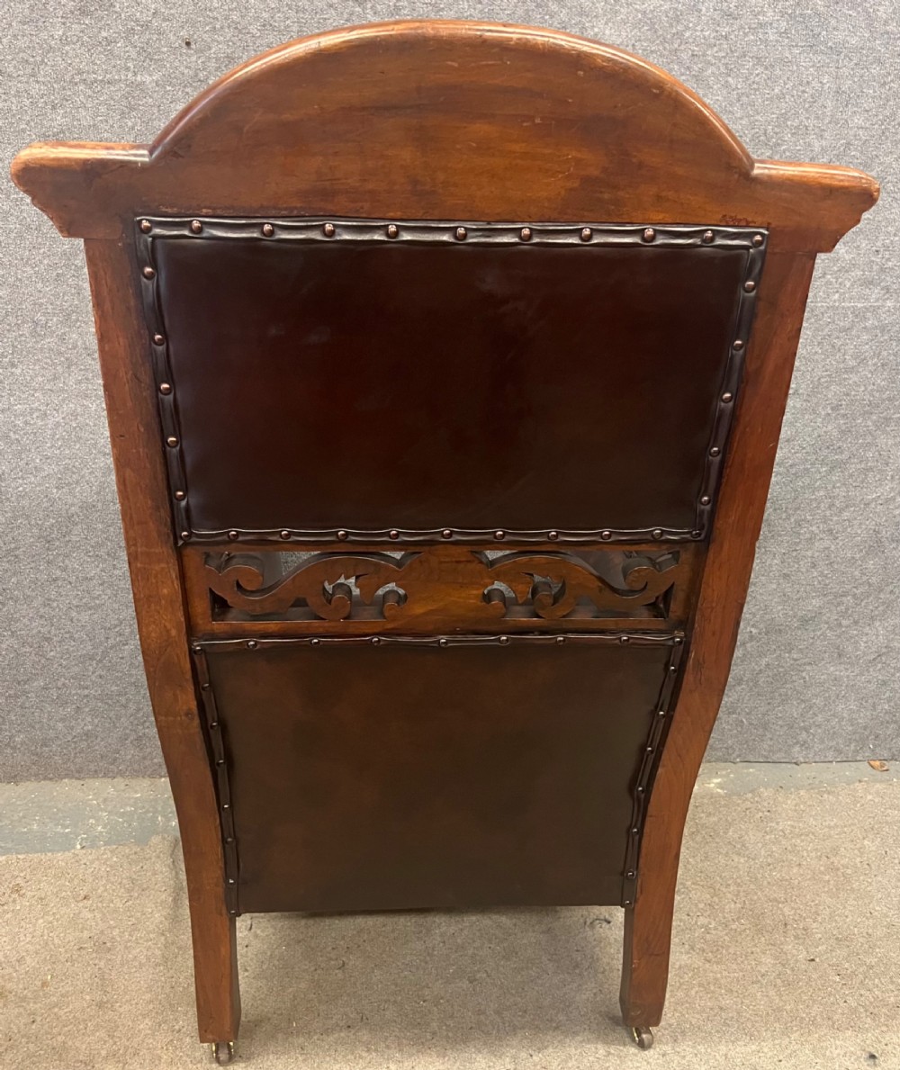 A pair of carved walnut high-back armchairs upholstered in dark brown leather with stud detailing and brass castors. View VII