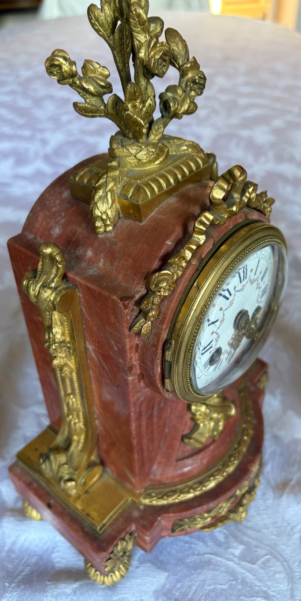 A three-piece French clock garniture featuring a central pink marble mantel clock decorated with gilt bronze floral mounts and flanked by two matching twin-light candelabra. View II