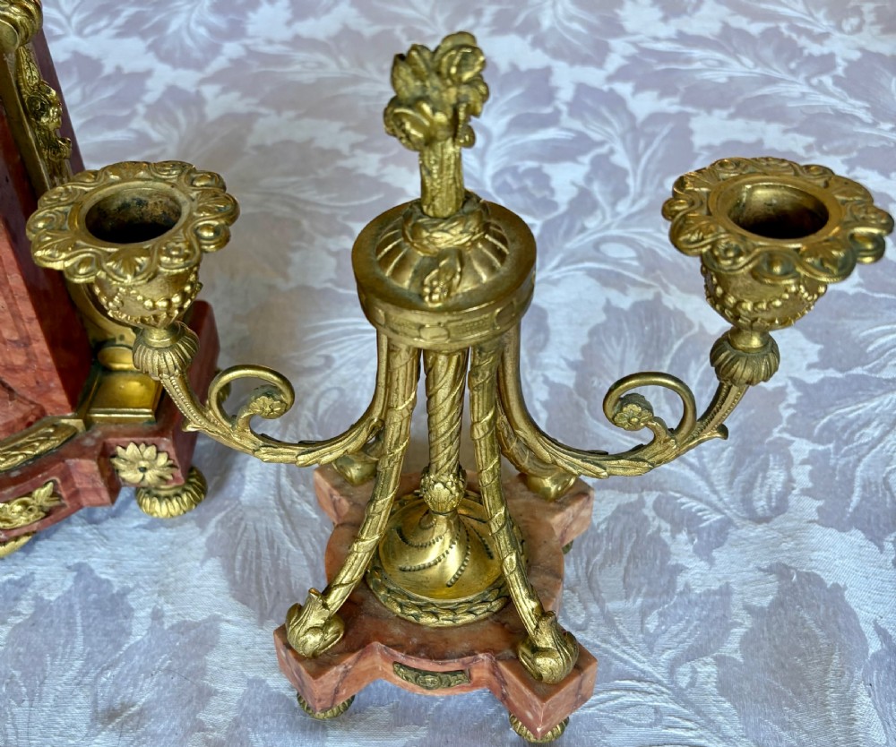 A three-piece French clock garniture featuring a central pink marble mantel clock decorated with gilt bronze floral mounts and flanked by two matching twin-light candelabra. View VIII