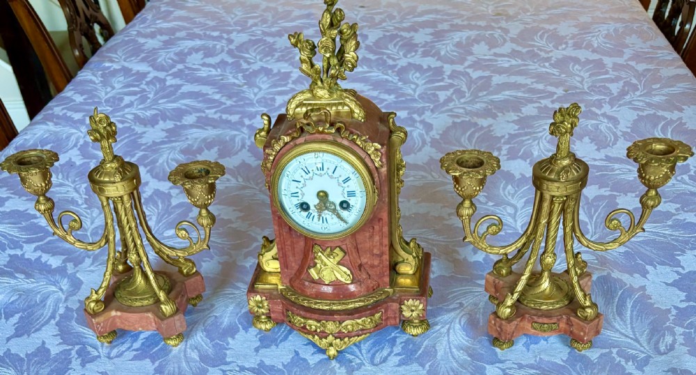 A three-piece French clock garniture featuring a central pink marble mantel clock decorated with gilt bronze floral mounts and flanked by two matching twin-light candelabra. View XI