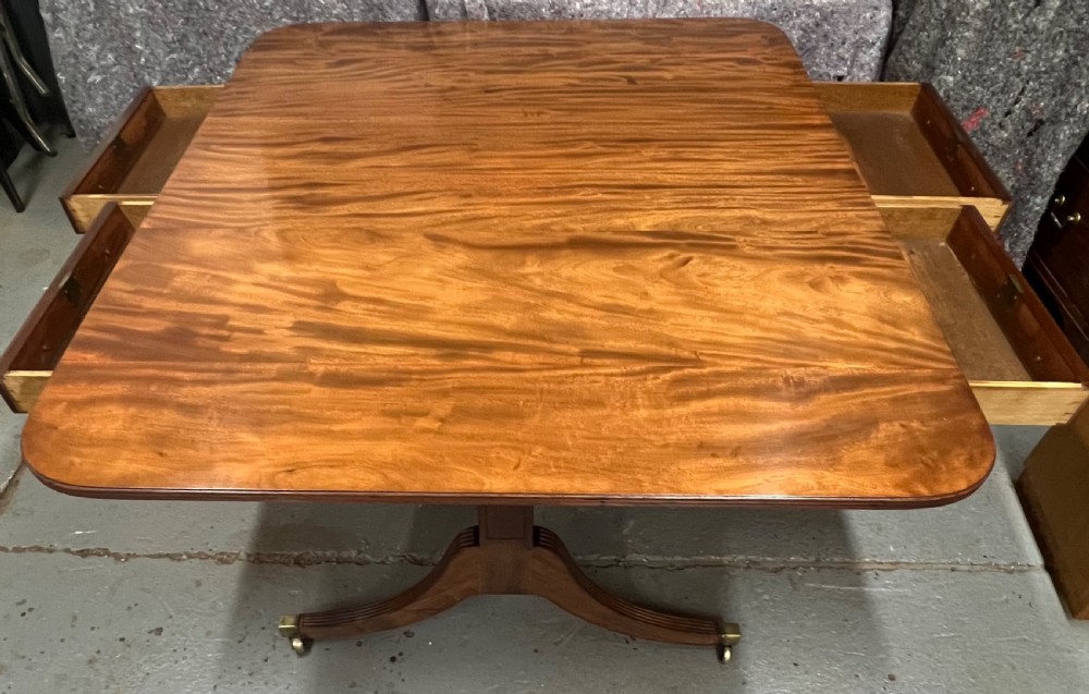 A mahogany library table featuring a flame veneer surface, frieze drawers with turned knobs, and reeded sabre legs resting on brass castors. View II