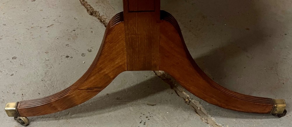 A mahogany library table featuring a flame veneer surface, frieze drawers with turned knobs, and reeded sabre legs resting on brass castors. View IV