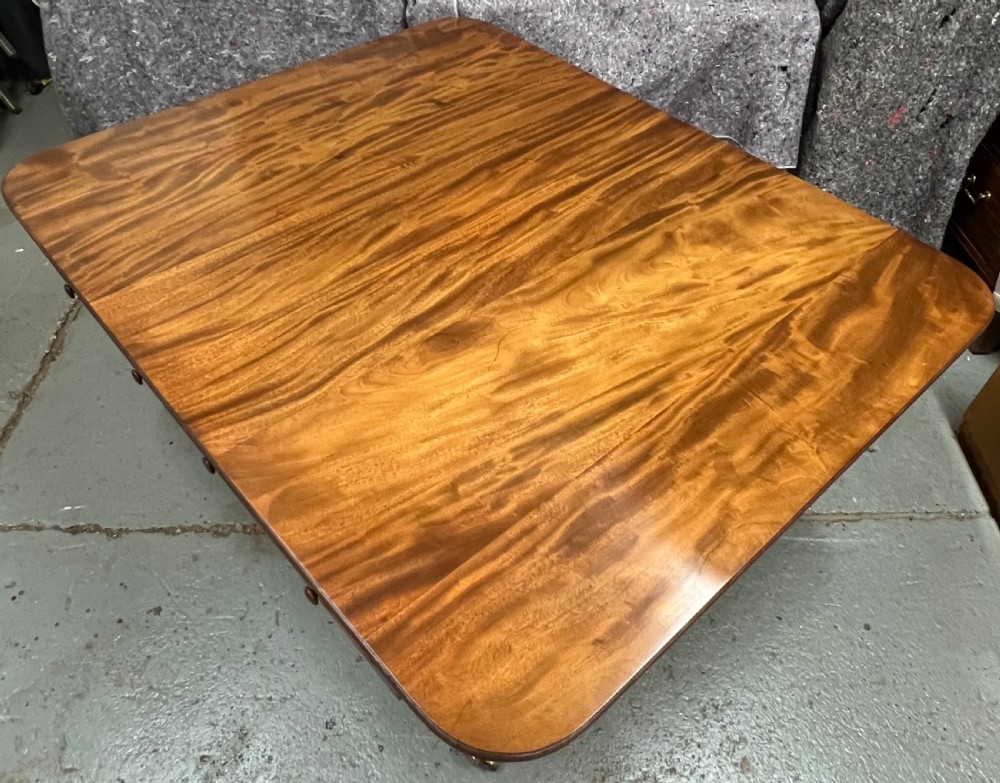 A mahogany library table featuring a flame veneer surface, frieze drawers with turned knobs, and reeded sabre legs resting on brass castors. View V