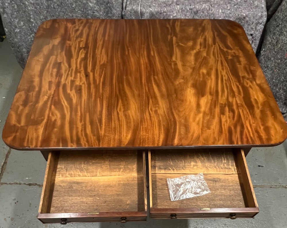 A mahogany library table featuring a flame veneer surface, frieze drawers with turned knobs, and reeded sabre legs resting on brass castors. View XII