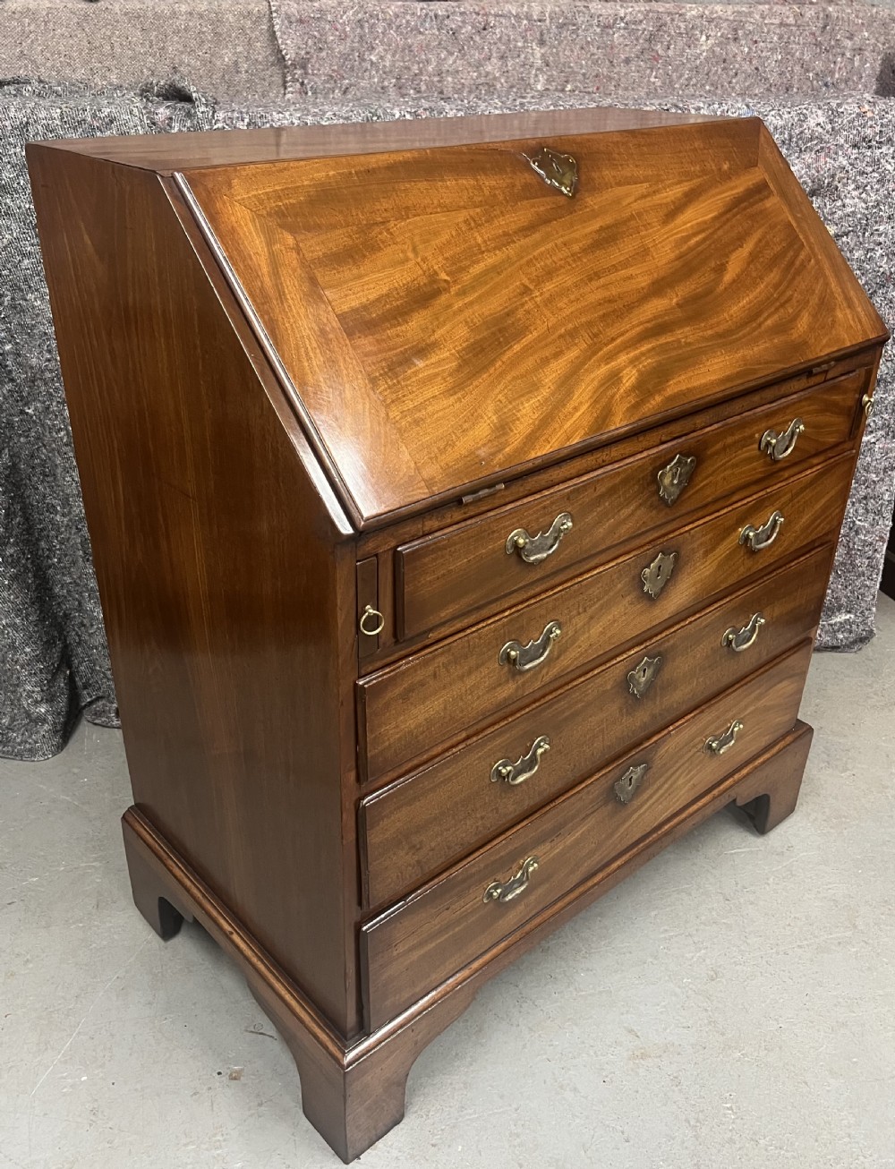 A small George II mahogany slant-front bureau featuring four graduated drawers with brass handles, resting on bracket feet.