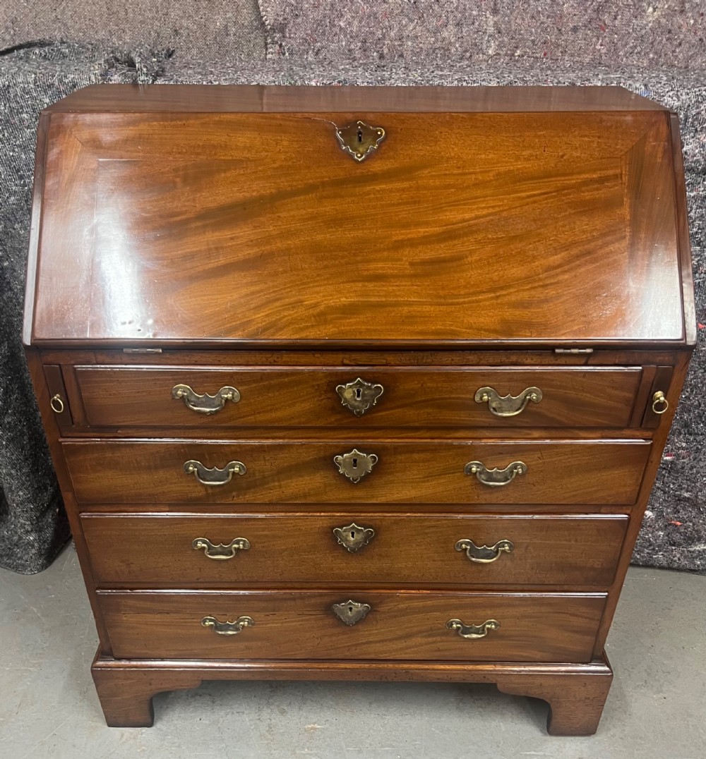 A small George II mahogany slant-front bureau featuring four graduated drawers with brass handles, resting on bracket feet. View III