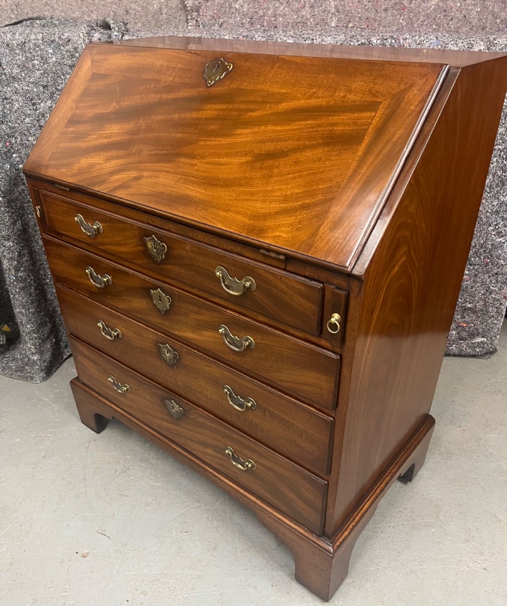 A small George II mahogany slant-front bureau featuring four graduated drawers with brass handles, resting on bracket feet. View VI