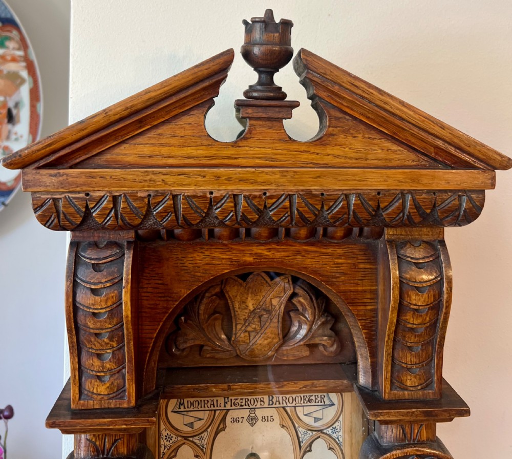 A 19th-century carved oak Admiral Fitzroy wall barometer featuring architectural details, an arched cresting, and a detailed paper weather register. View II
