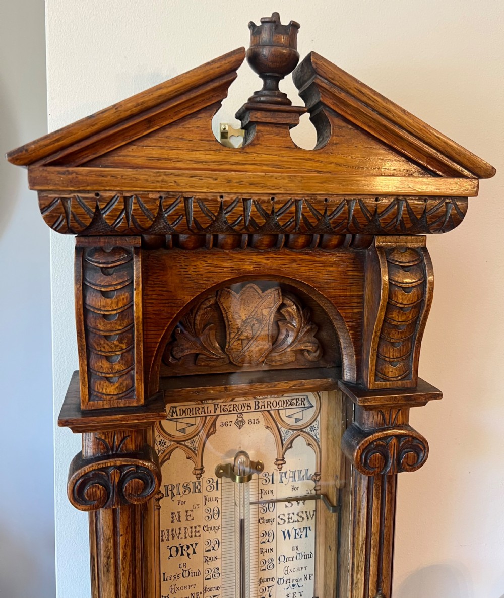 A 19th-century carved oak Admiral Fitzroy wall barometer featuring architectural details, an arched cresting, and a detailed paper weather register. View IV