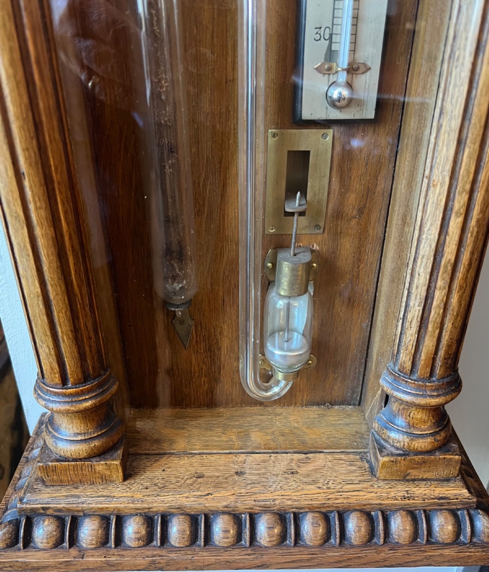 A 19th-century carved oak Admiral Fitzroy wall barometer featuring architectural details, an arched cresting, and a detailed paper weather register. View VI