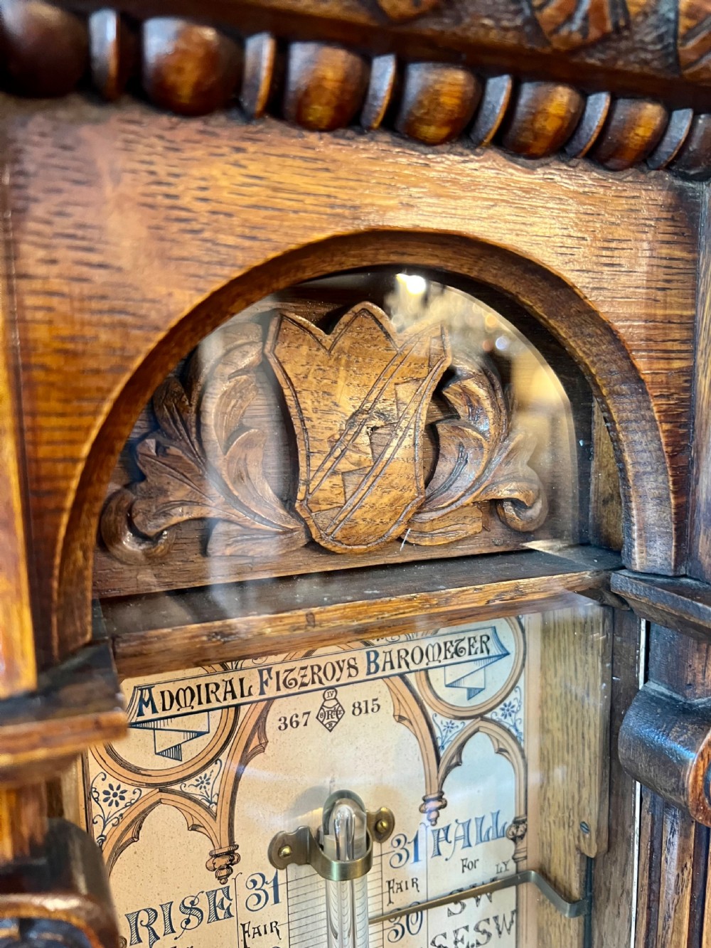 A 19th-century carved oak Admiral Fitzroy wall barometer featuring architectural details, an arched cresting, and a detailed paper weather register. View IX