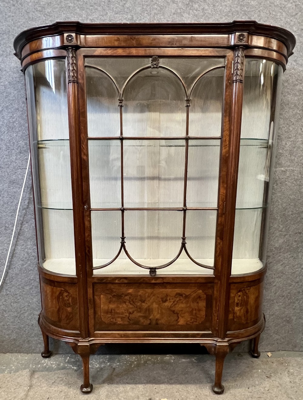 An Edwardian burr walnut display cabinet featuring curved glass side panels, an astragal glazed central door, glass shelves, and cabriole legs. View II