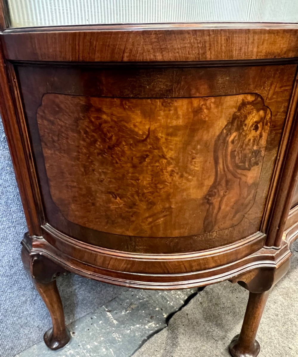 An Edwardian burr walnut display cabinet featuring curved glass side panels, an astragal glazed central door, glass shelves, and cabriole legs. View IV