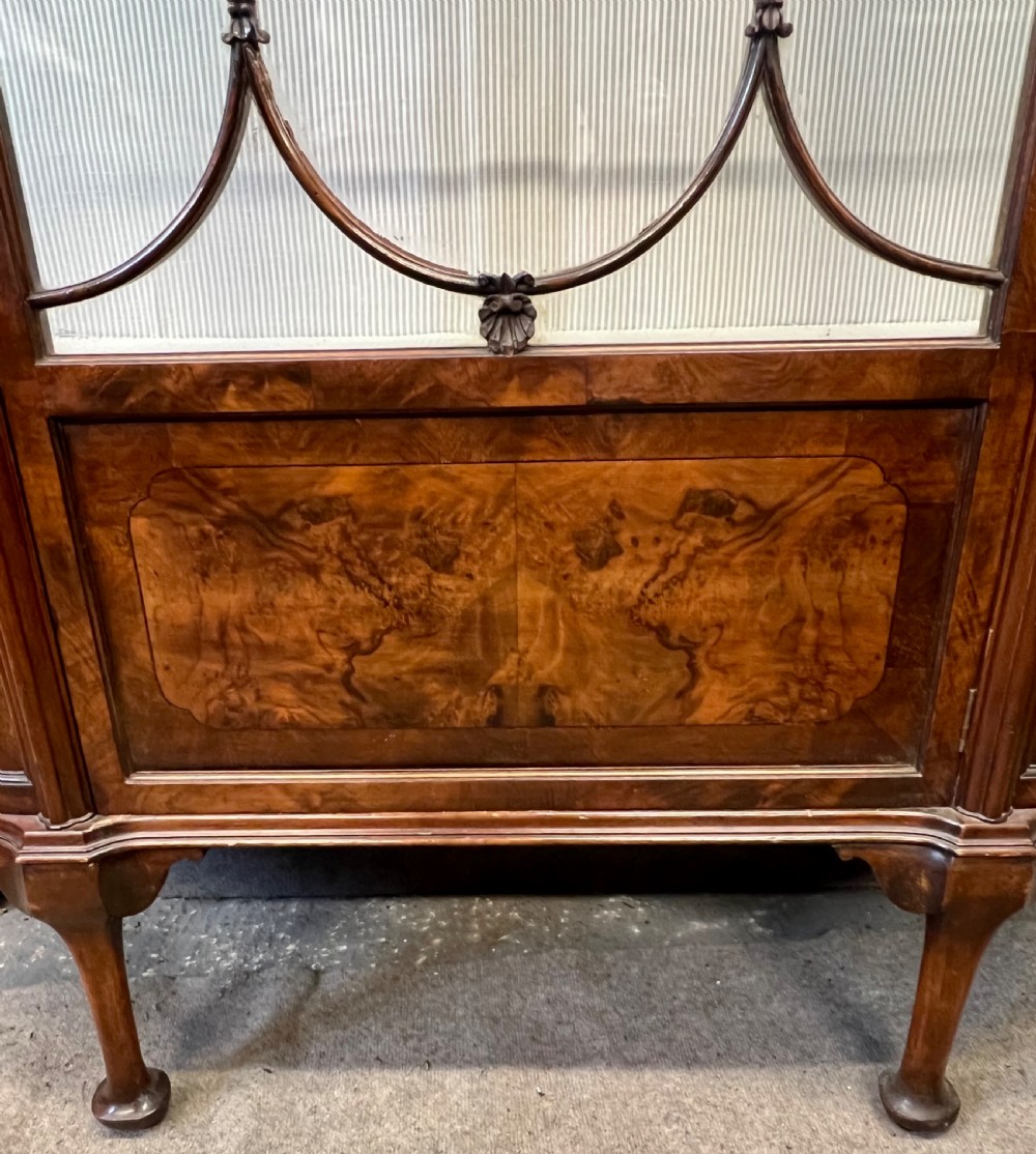 An Edwardian burr walnut display cabinet featuring curved glass side panels, an astragal glazed central door, glass shelves, and cabriole legs. View VII