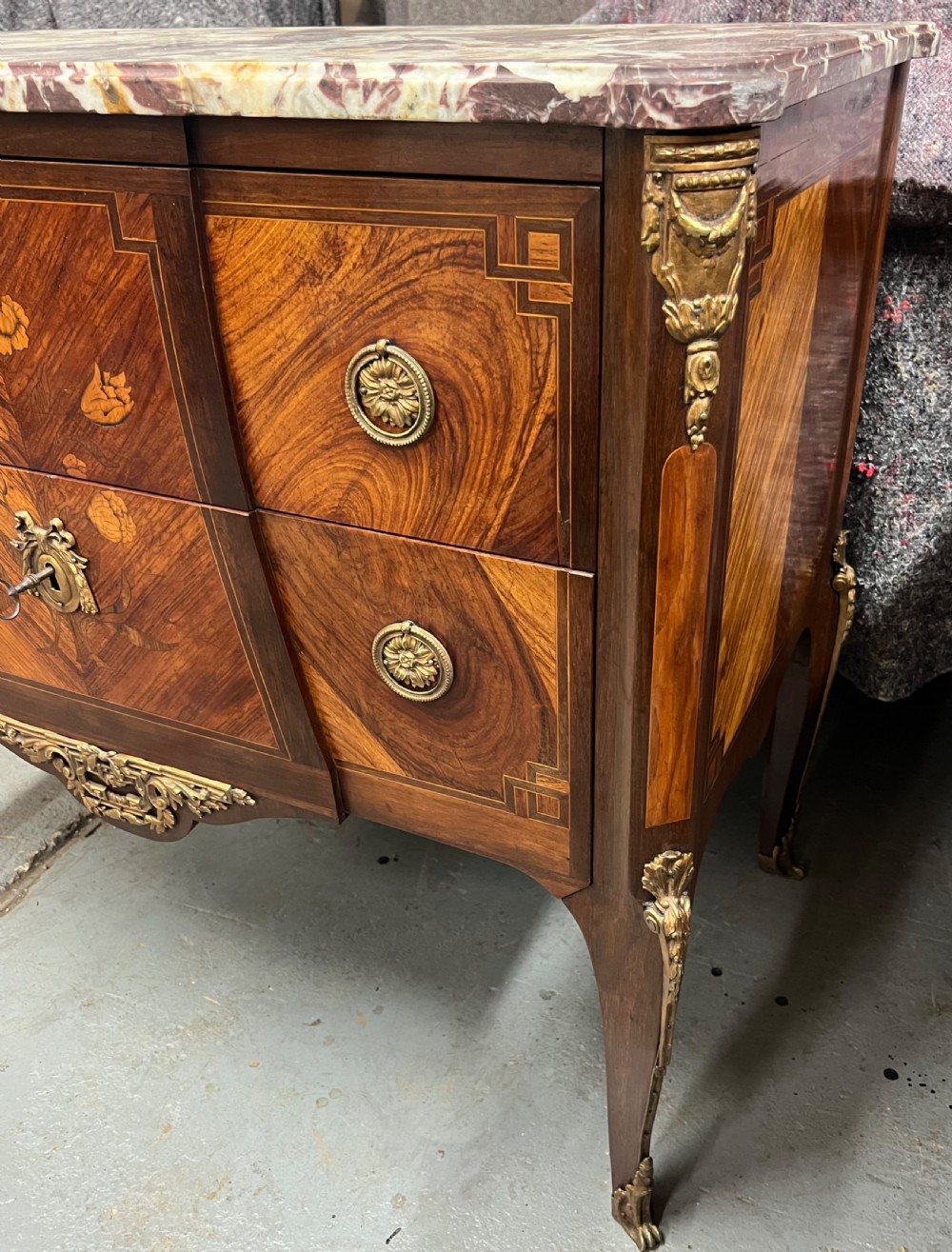 A nineteenth-century French Louis XV style commode with a contoured marble top, intricate floral marquetry, twin drawers, and cast gilt-bronze ormolu mounts. View XII