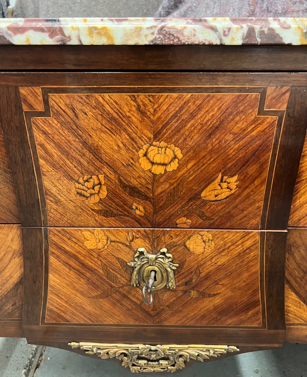 A nineteenth-century French Louis XV style commode with a contoured marble top, intricate floral marquetry, twin drawers, and cast gilt-bronze ormolu mounts. View XIII