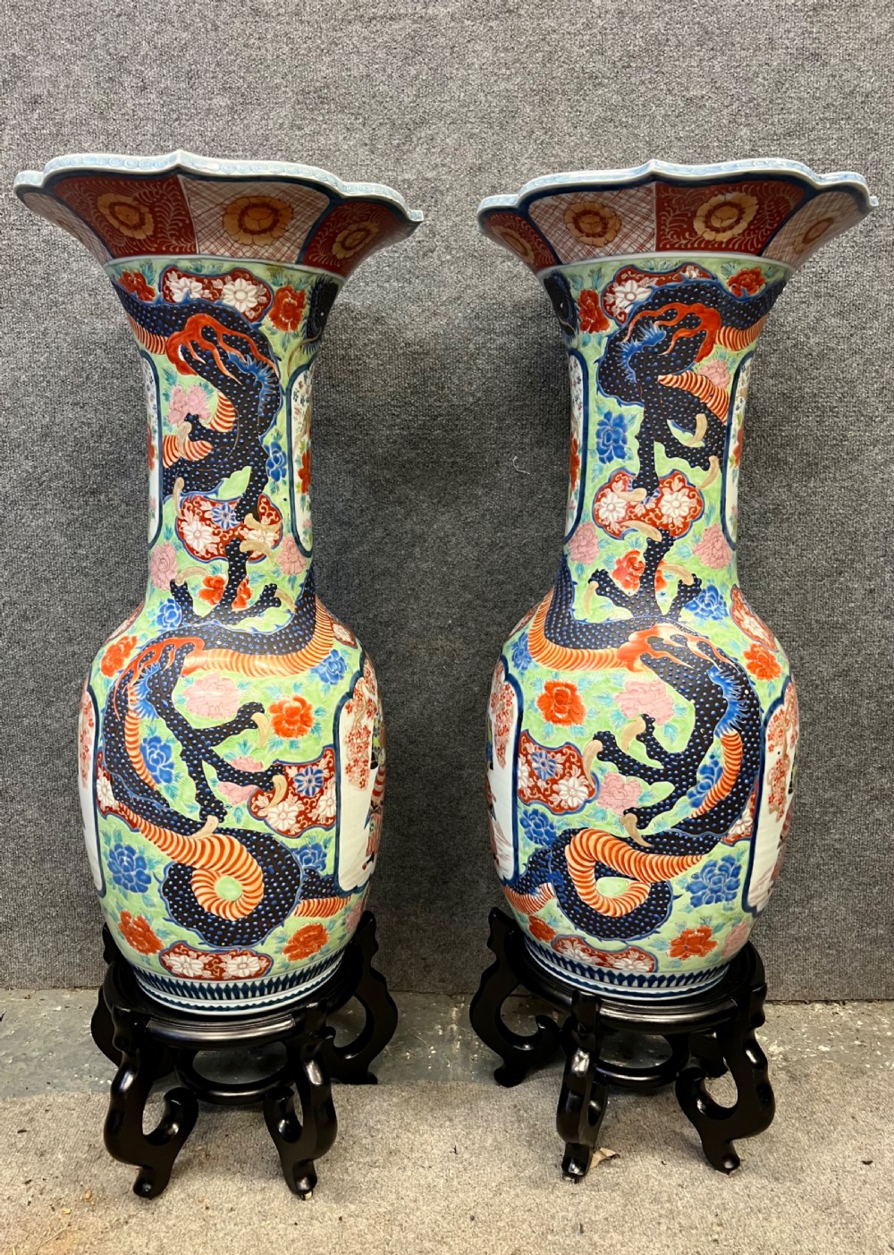A pair of large, baluster-shaped Arita porcelain floor vases decorated with polychrome figures, floral motifs, and dragons, supported on carved dark wood bases. View II