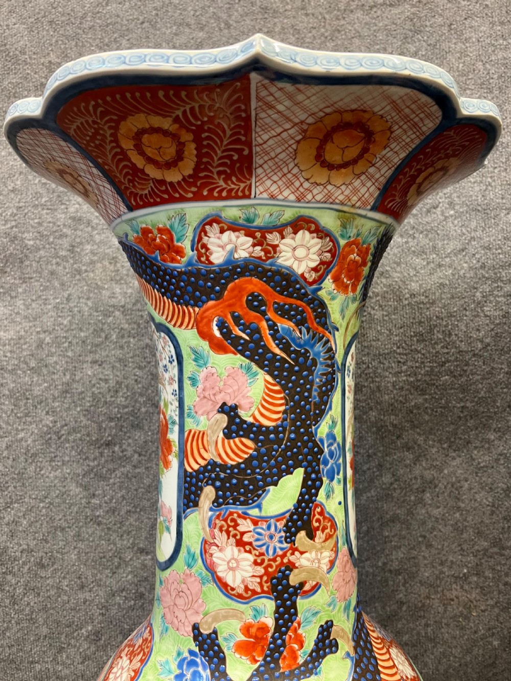 A pair of large, baluster-shaped Arita porcelain floor vases decorated with polychrome figures, floral motifs, and dragons, supported on carved dark wood bases. View V