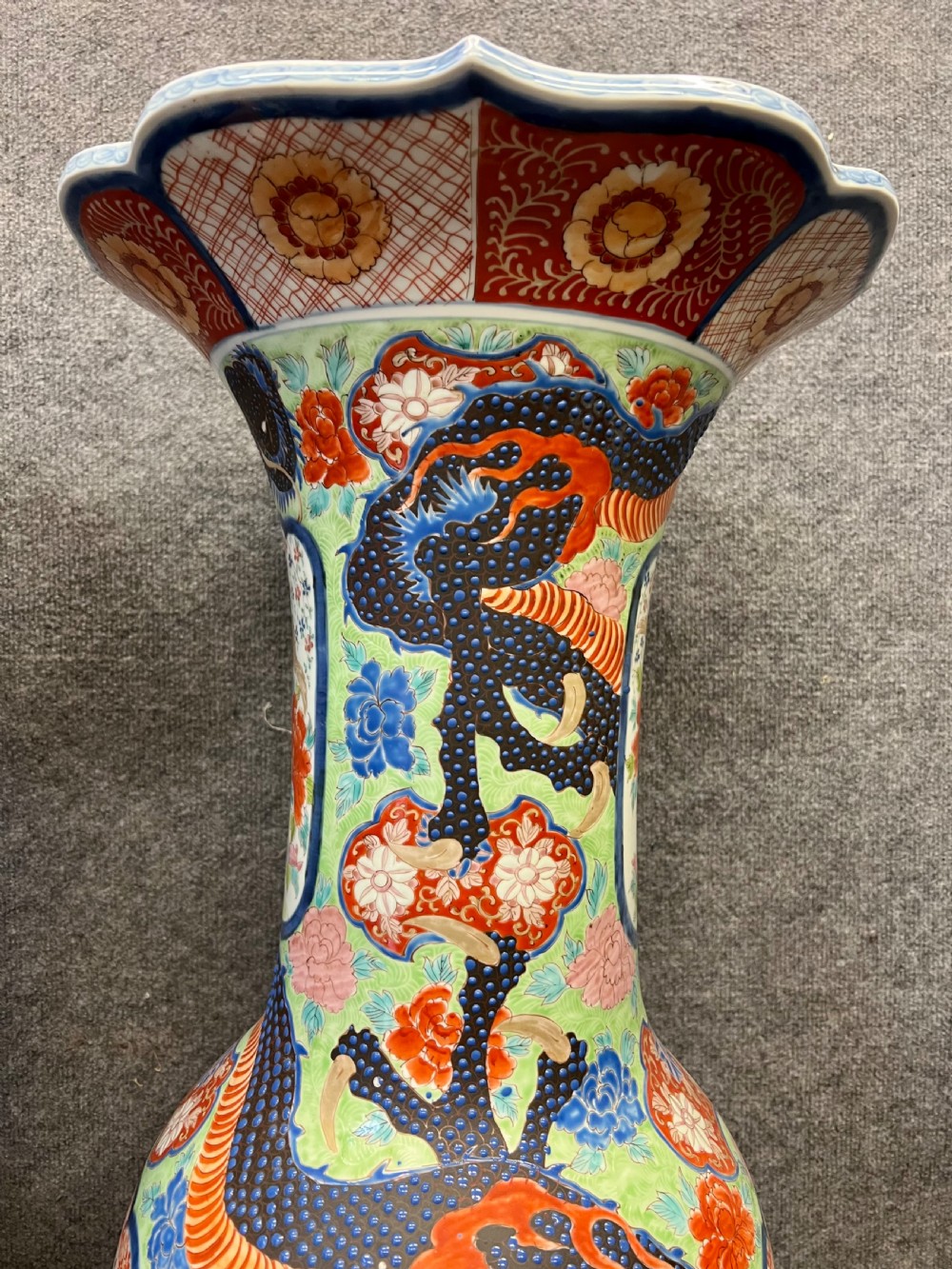 A pair of large, baluster-shaped Arita porcelain floor vases decorated with polychrome figures, floral motifs, and dragons, supported on carved dark wood bases. View VI